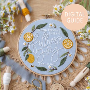 Puede incluir: Un bastidor de bordado azul claro con la frase bordada "In your presence there is fullness of joy". El diseño incluye limones amarillos, hojas verdes y flores blancas. También se incluye el texto "Salmo 16:11".