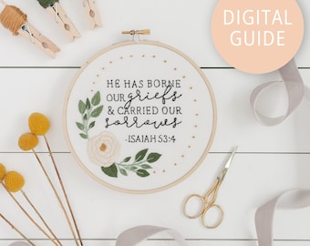 May include: White embroidery hoop with a floral design and the text "He has borne our griefs & carried our sorrows - Isaiah 53:4".