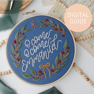 May include: Embroidered hoop art with the text "O come, O come, Emmanuel" in white thread on a blue background. The design includes green leaves, red berries, a gold star, and a gold bow. The words "DIGITAL GUIDE" are in a peach circle.