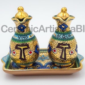 Puede incluir: Dos jarras de cerámica doradas con diseños de mosaico azul y verde, etiquetadas como "Vino" y "Acqua", sobre una bandeja dorada con un diseño de mosaico.