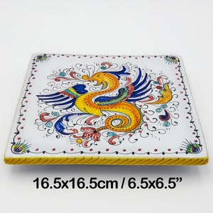 Puede incluir: Plato decorativo cuadrado de cerámica, 16,5 x 16,5 cm, con un diseño de criatura mítica amarilla, azul y naranja. El plato blanco tiene un borde amarillo y detalles florales. Una pieza única para la decoración del hogar.