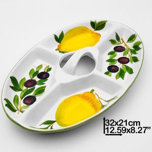Puede incluir: Plato de servir de cerámica blanca con cuatro secciones, con un diseño de limón y rama de olivo. El plato tiene un asa y mide 32 x 21 cm.