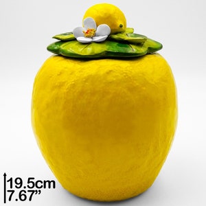 Peut inclure: Un pot en céramique jaune en forme de citron avec un couvercle en feuille verte et fleur blanche. Le pot mesure 19,5 cm de haut.