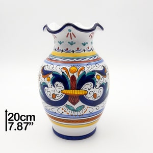 May include: A white ceramic vase with a scalloped rim and a colorful floral design. The vase is 7.87 inches tall and features blue, yellow, red, and green accents.