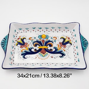 Op de afbeelding: Een wit keramisch dienblad met blauwe, gele en rode bloemmotieven. Het dienblad heeft twee handvatten en meet 34 x 21 cm.