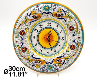 May include: A round wall clock with a diameter of 11.81 inches, featuring a central yellow circle surrounded by a white face with black numerals. The border is decorated with intricate blue, yellow, and red floral and mythical creature motifs.