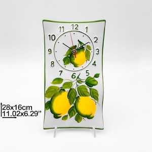 May include: White ceramic clock with a green border and a lemon design. The clock face has black hands and green numbers. The clock is 11.02 inches by 6.29 inches.