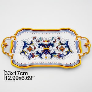 Könnte beinhalten: Ein weißes Keramik-Serviertablett mit blauen, gelben und roten Blumendesigns. Das Tablett hat zwei Griffe und misst 33 x 17 cm.