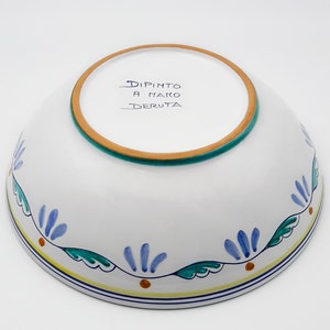 May include: White ceramic bowl with a blue and green floral design around the rim. The bottom of the bowl is marked "Dipinto a Mano Deruta".