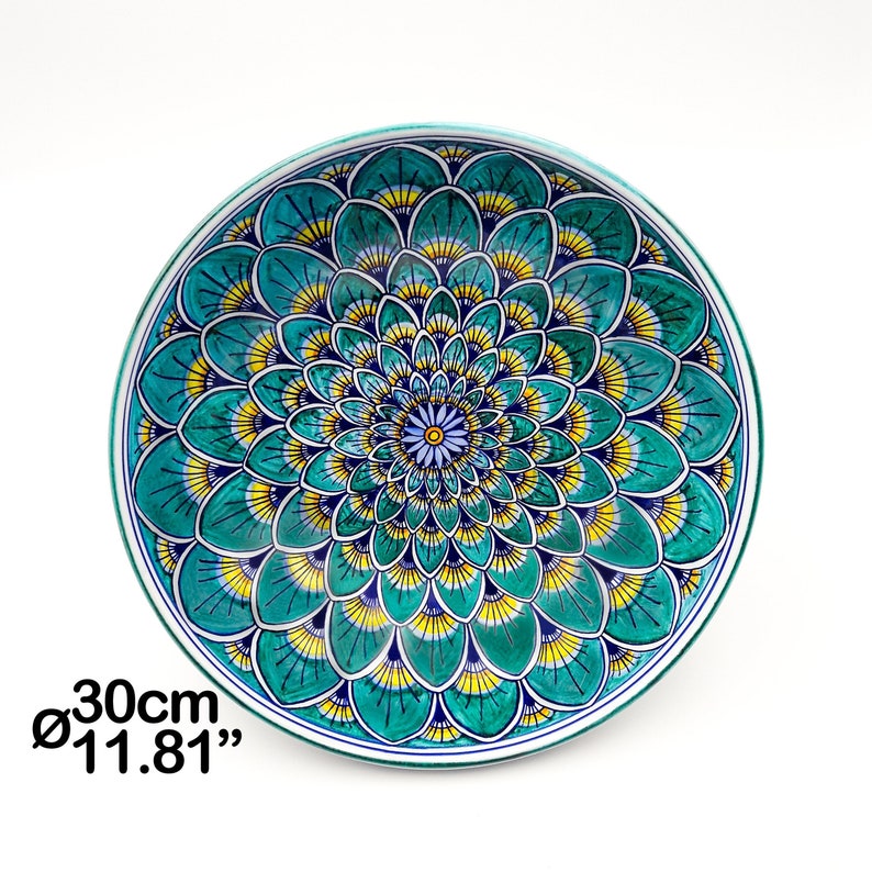 May include: A large, round ceramic plate with a green, yellow, and blue floral design. The plate measures 11.81 inches in diameter.