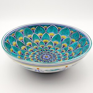 May include: A large, white ceramic bowl with a blue and green floral design. The bowl has a scalloped edge and a white interior.