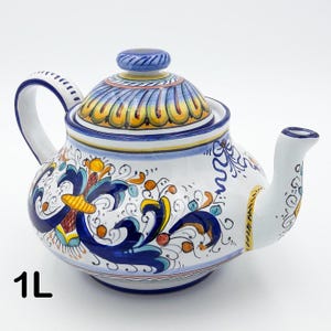 Può includere: Teiera in ceramica bianca con coperchio, manico e beccuccio. La teiera è decorata con motivi floreali blu, gialli e arancioni. La teiera ha una capacità di 1L.