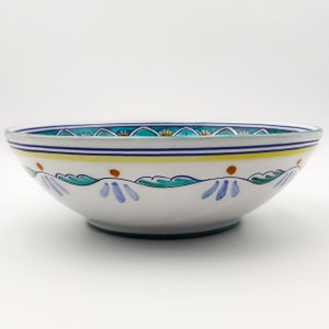 May include: A large, white ceramic bowl with a blue, green, and yellow floral design. The bowl is oval shaped and has a wide rim.