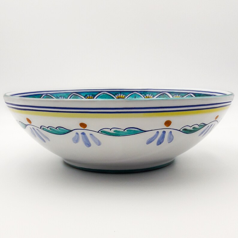 May include: A large, white ceramic bowl with a blue, green, and yellow floral design. The bowl is oval shaped and has a wide rim.