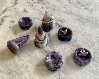 May include: Seven amethyst ring and earring holders in various shapes, including cones and bowls. The holders are made of polished amethyst and have a purple and white swirl pattern.