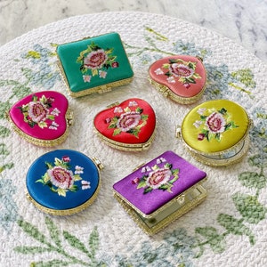 Pode incluir: Sete espelhos compactos florais bordados em várias cores e formas. Os espelhos são em forma de coração, redondos e retangulares. Os desenhos florais são em tons de rosa, vermelho, amarelo e verde.