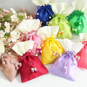 May include: Assortment of colourful satin drawstring bags with decorative knots and tassels. The bags are in various colours, including pink, yellow, blue, green, and red.