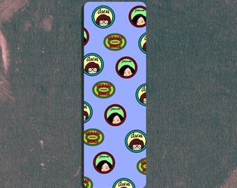 May include: A rectangular bookmark with a light blue background. The bookmark is decorated with circular illustrations of cartoon faces with the names "Daria" and "Jane" written around them. The background is a dark, textured surface.
