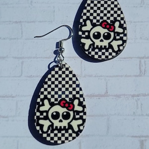 May include: A pair of black and white checkered teardrop shaped earrings with a white skull and red bow design.