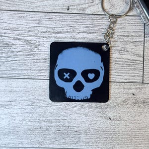 Pu&ograve; includere: Un portachiavi a forma di teschio nero e blu con una croce per un occhio e un cuore per l'altro occhio.
