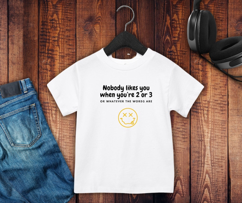 May include: White t-shirt with a black graphic that says "Nobody likes you when you're 2 or 3 or whatever the words are" and a yellow smiley face with two X's for eyes.