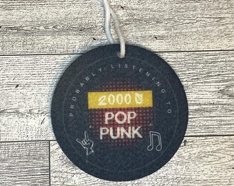 May include: Black and white round tag with white text that reads "Probably listening to 2000's Pop Punk" with a yellow rectangle behind the 2000's. The tag has a white string attached to it.