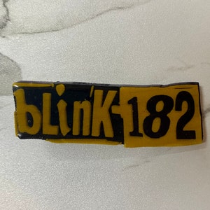 May include: Black and gold rectangular sticker with the text "blink 182" in black.