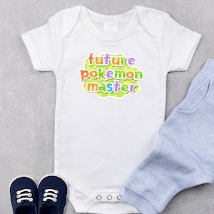 May include: White baby onesie with the text "future pokemon master" in colorful letters. Light blue baby pants and navy blue shoes are also in the image. The onesie has three snaps at the bottom.