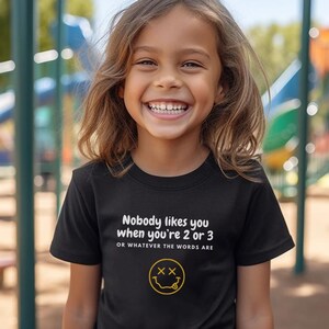 May include: A black t-shirt with white text that reads "Nobody likes you when you're 2 or 3 or whatever the words are" and a yellow smiley face with two X's for eyes.