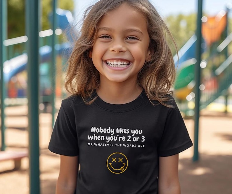 May include: A black t-shirt with white text that reads "Nobody likes you when you're 2 or 3 or whatever the words are" and a yellow smiley face with two X's for eyes.