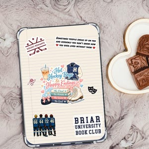 May include: A clear tablet case with stickers featuring hockey-themed graphics and text. Stickers include "Hockey Romance," "Hot Hockey Boys & Happy Endings," and "Briar University Book Club." The case is on a textured, light-colored surface.