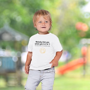 May include: White toddler t-shirt with black text that reads "Nobody likes you when you're 2 or 3 or whatever the words are" and a yellow smiley face with an X for eyes.