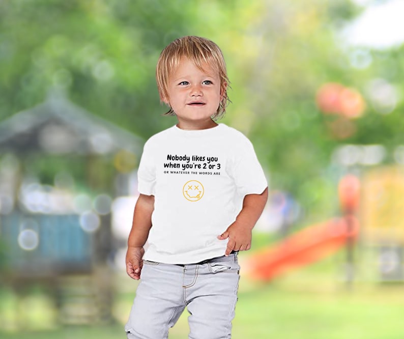 May include: White toddler t-shirt with black text that reads "Nobody likes you when you're 2 or 3 or whatever the words are" and a yellow smiley face with an X for eyes.