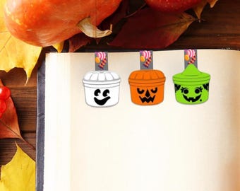 May include: Three magnetic bookmarks featuring Halloween designs. One is a white ghost, one is an orange jack-o'-lantern, and one is a green monster. Each bookmark has a small tab at the top displaying a colorful candy graphic on a gray background.