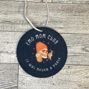 May include: Black and white round ornament with the text "Emo Mom Club It Was Never A Phase" and a cartoon skeleton wearing a beanie holding a cup of coffee.