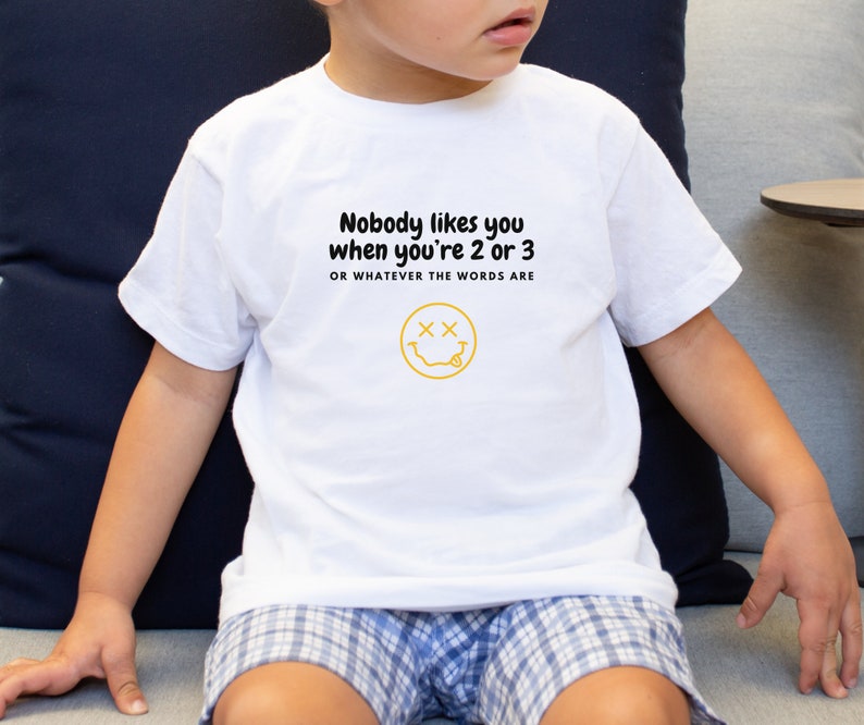 May include: White t-shirt with a black graphic that says "Nobody likes you when you're 2 or 3 or whatever the words are" and a yellow smiley face with x's for eyes.