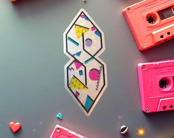 May include: A holographic sticker featuring the iconic "S" design, filled with geometric shapes in pink, yellow, blue, and purple. The sticker is surrounded by colorful cassette tapes in shades of pink, orange, and teal, set against a gray background.