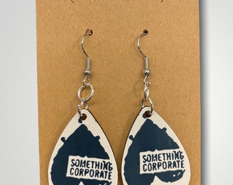 May include: A pair of white teardrop-shaped earrings with black and white text that reads "Something Corporate" on each earring.