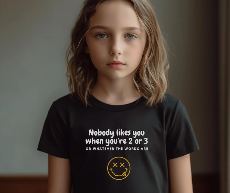 May include: Black t-shirt with white text that reads "Nobody likes you when you're 2 or 3 or whatever the words are" and a yellow smiley face with an X for eyes.