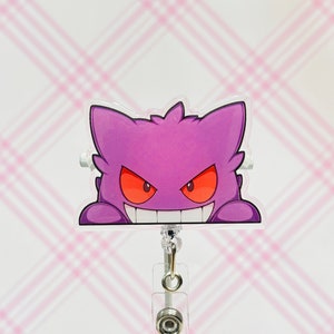 May include: A purple and red cartoon ghost character with a menacing grin, peeking out from behind a clear plastic badge holder. The badge holder is attached to a silver retractable badge reel.
