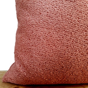 May include: A close-up of a soft, plush pillow with a textured, peach-colored fabric.