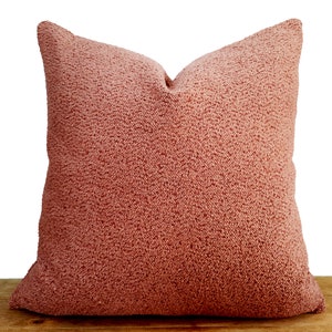 May include: A soft, plush pillow with a fuzzy, peach-colored fabric. The pillow is square-shaped and has a simple design.