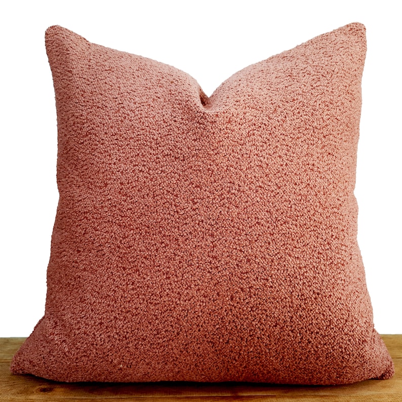 May include: A soft, plush pillow with a fuzzy, peach-colored fabric. The pillow is square-shaped and has a simple design.