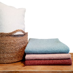 May include: A woven basket with a white pillow on top, next to a stack of three blankets in blue, pink, and red.