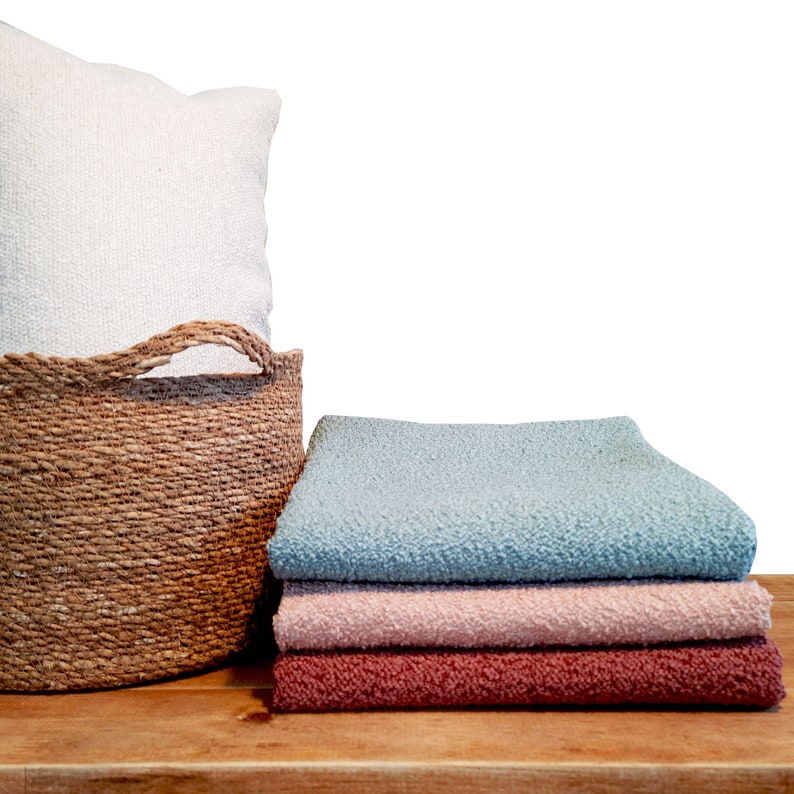 May include: A woven basket with a white pillow on top, next to a stack of three blankets in blue, pink, and red.