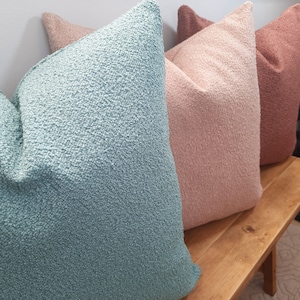 May include: Three decorative throw pillows in different colors. The pillow on the left is a light blue, the middle pillow is a light pink, and the pillow on the right is a light brown.