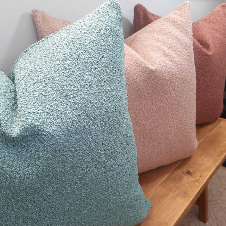 May include: Three decorative throw pillows in different colors. The pillow on the left is a light blue, the middle pillow is a light pink, and the pillow on the right is a light brown.