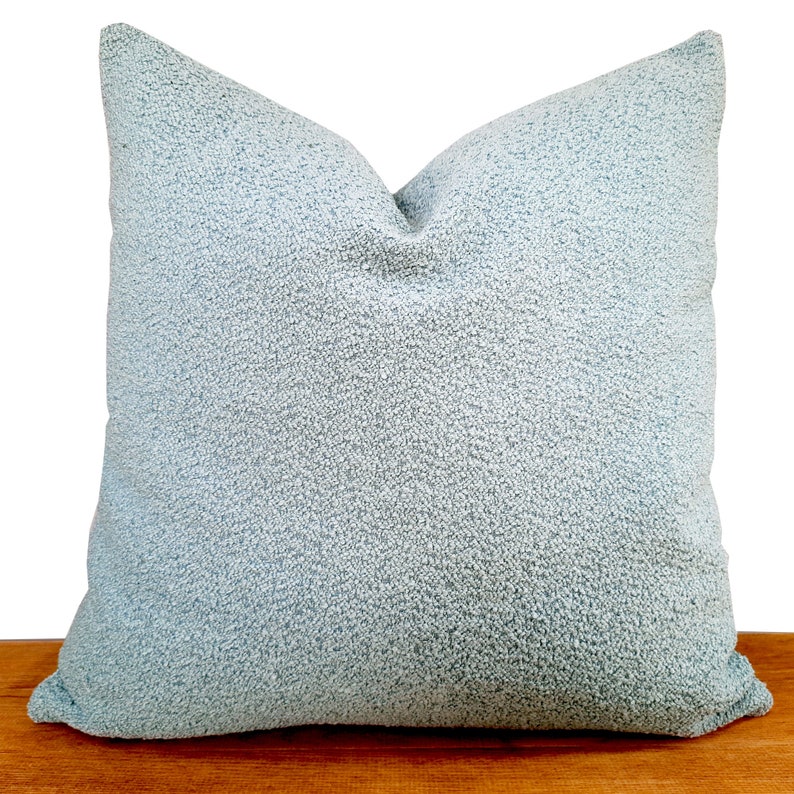 May include: A light blue throw pillow with a soft, textured fabric. The pillow is square shaped and has a subtle sheen.