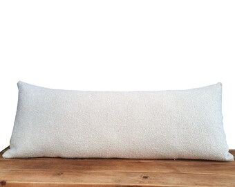 May include: A white, rectangular lumbar pillow with a textured fabric surface. The pillow is resting on a wooden bench.