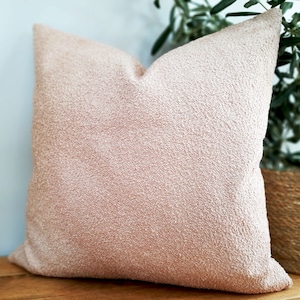 May include: A soft, plush pink throw pillow with a textured surface. The pillow is made of a fuzzy material and has a square shape.